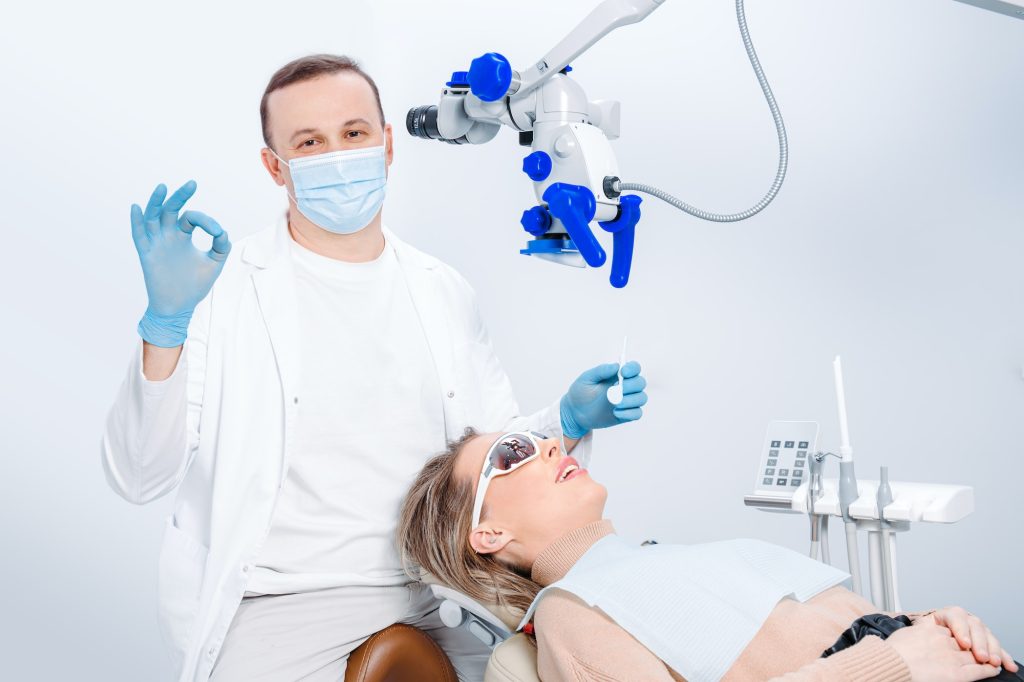 Male dentist examining patient looking on the teeth with professional microscope at surgery